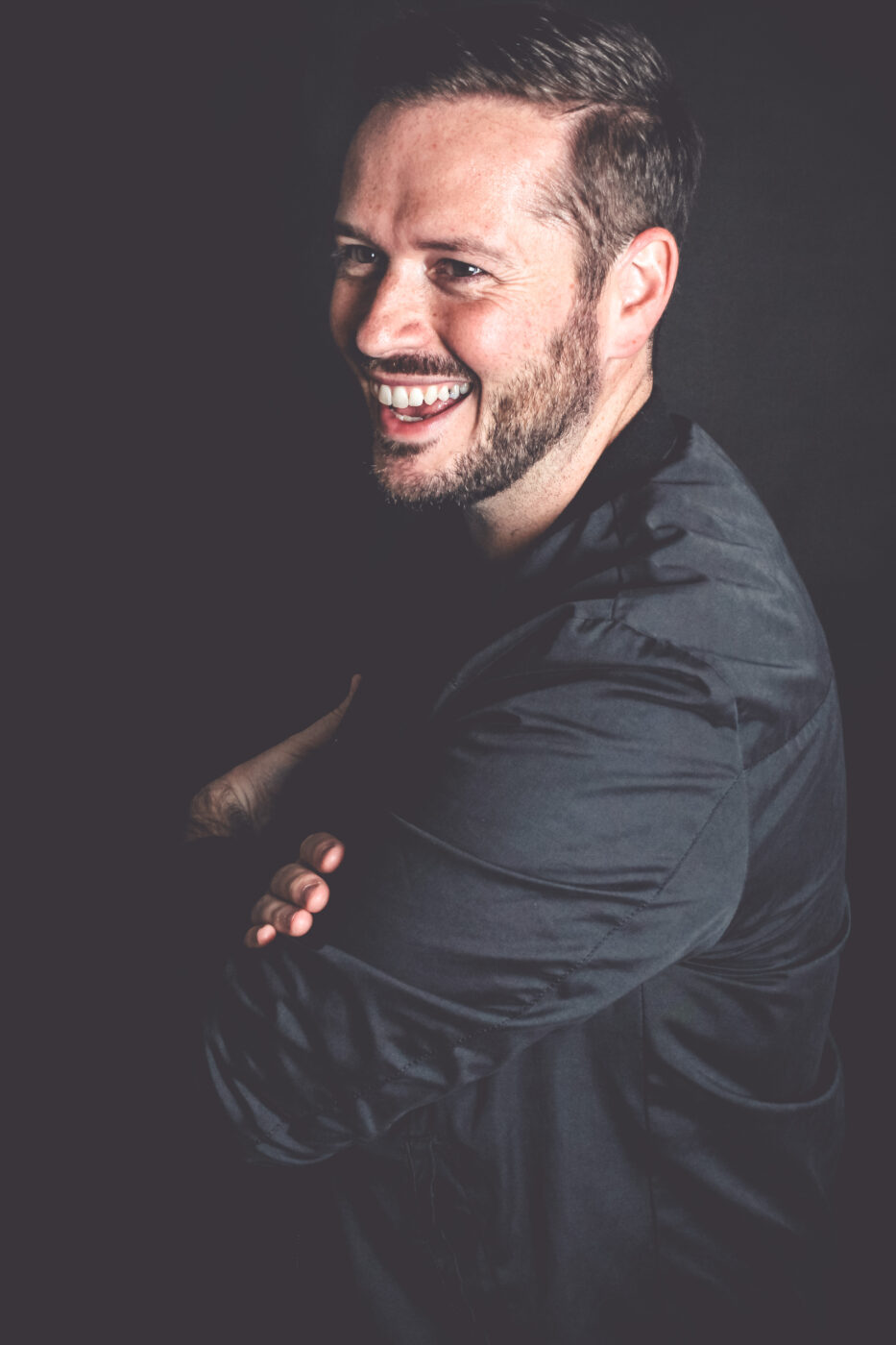 Bild von Benjamin Schäfer als Portrait mit verschränkten Armen vor der Brust und einem strahlenden Lächeln, sehr einladend und fröhlich