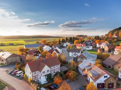 Idyllisches Dorf in herbstlicher Landschaft mit Fachwerkhäusern und grünen Feldern unter blauem Himmel
